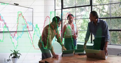 Collaborating team analyzing market charts around table with laptops in modern workspace