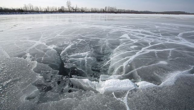 Fracturing frozen lake revealing deep hole and radiating white cracks across icy expanse
