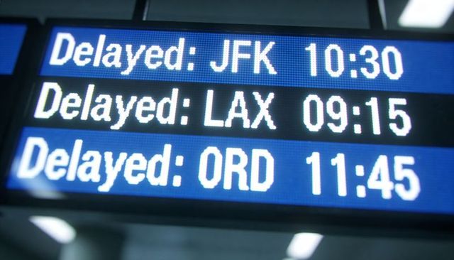 Blue LED departure board showing delayed flights to JFK, LAX, ORD with clear digital times
