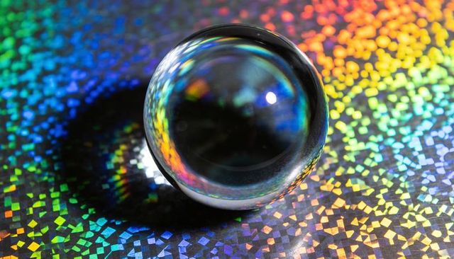 Glass sphere refracting rainbow mosaic on holographic surface, macro prism abstract