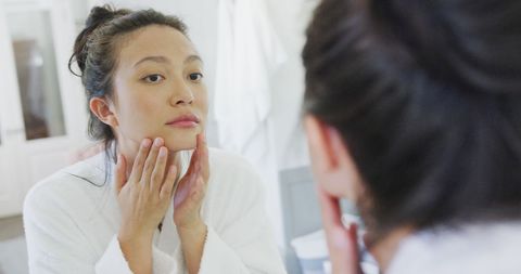 Young woman in bathrobe checking skin health in mirror