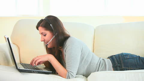 Young Woman Using Laptop and Headset Relaxing on Couch