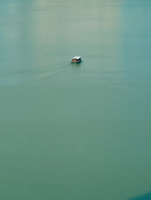 This picture captures a single boat floating on calm aquamarine waters. Ideal for travel and adventure blogs, promotional material for relaxation retreats, peaceful meditation content, and evocative storytelling purposes.