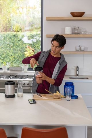 Young asian man preparing morning smoothie at sunlit modern kitchen island with blender