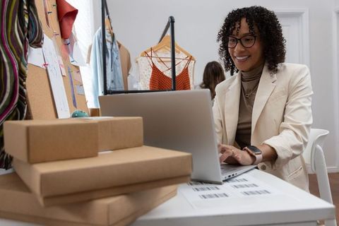 African american entrepreneur packing orders and typing on laptop for online store