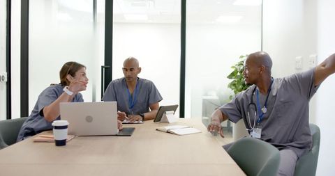 Medical team collaborating over laptop and tablet in clinic meeting room for care planning