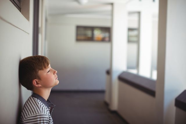 Close-up of sad schoolboy leaning head against wall in corridor of school