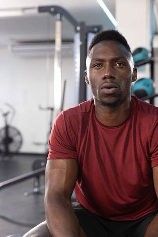 African american man resting on gym bench after intense strength workout, catching breath