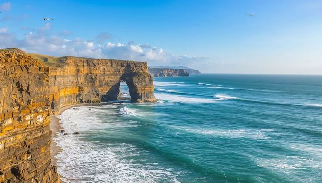 Framing sea arch on golden layered cliffs with turquoise ocean waves and soaring seabirds