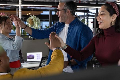Diverse team celebrating milestone with high fives in modern open-plan office workspace