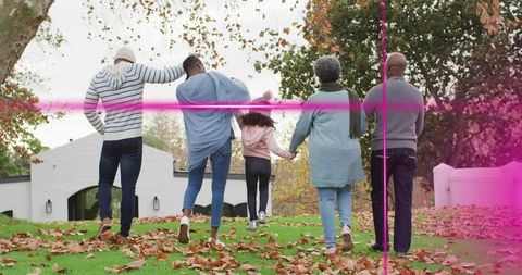 Multigenerational family walking uphill linking arms toward white suburban house in autumn