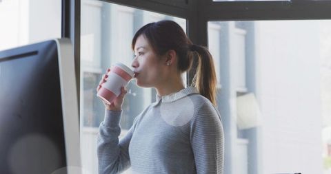 Woman Drinking from Travel Cup in Urban Office Workspace