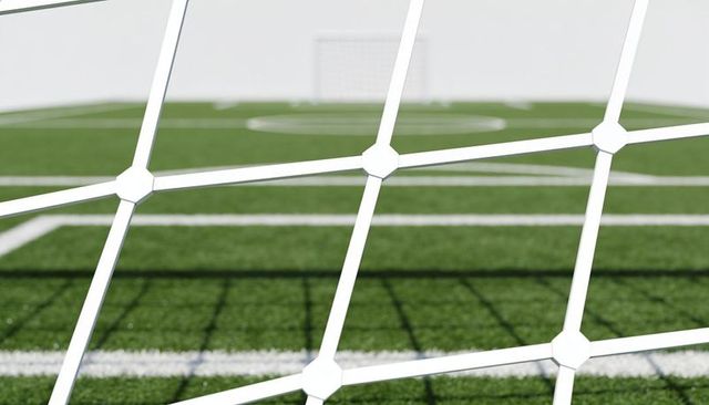 Closeup white soccer goal net framing blurred artificial turf and field lines, shadow