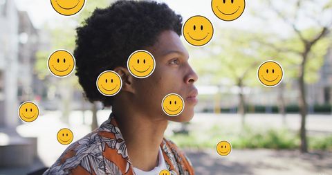 Thoughtful Young Man Surrounded by Smiley Emojis Outdoors