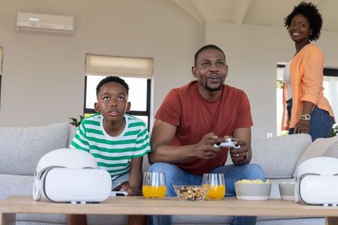 African american family playing video games with controllers and vr headsets on sofa