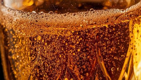 Macro showcasing effervescent amber drink in faceted tumbler with rising bubbles