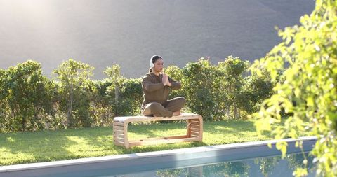 Woman Meditating with Headphones by Tranquil Poolside Setting