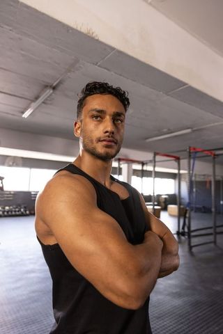 Muscular man standing with arms crossed in gym showing strength determination and focus