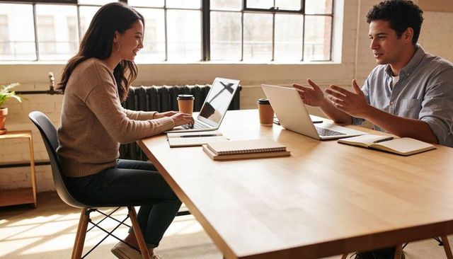 Young professionals collaborating over laptops at bright modern industrial workspace