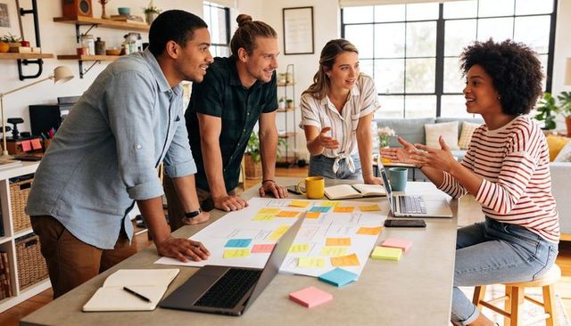 Diverse creative team collaborating and brainstorming around table with sticky notes and laptops