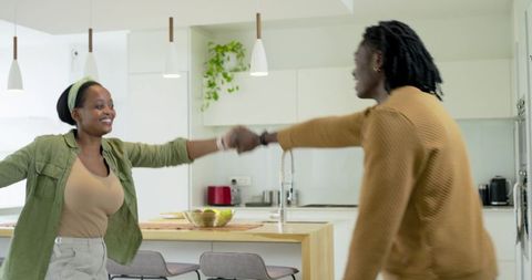African American couple holding hands and smiling while turning at modern kitchen island