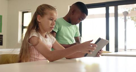 Multicultural elementary students sharing tablet, collaborating on classroom learning