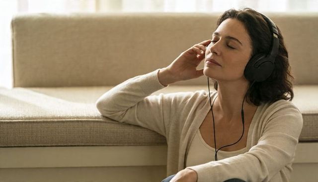 Woman listening to music with headphones, relaxing mindfully at home by sofa