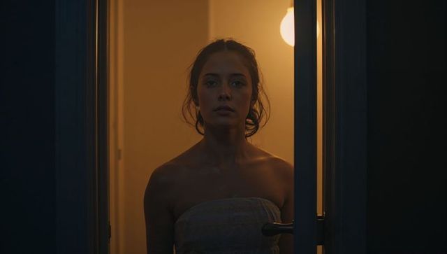 Backlit woman standing in doorway wrapped in towel with warm amber interior light