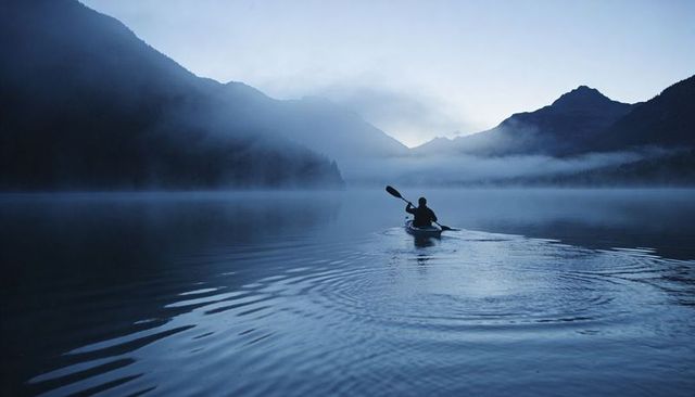Solo kayaker paddling through misty alpine lake at dawn