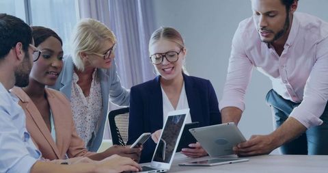 Multiracial Business Team Collaborating Over Laptops, Tablets and Phones in Bright Office