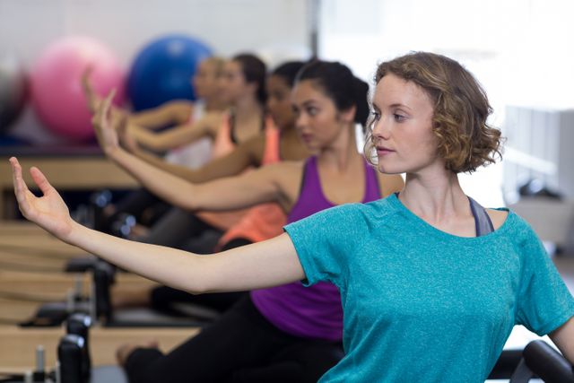 Women participating in a group Pilates class using reformers in a gym. They are focused on their movements, emphasizing balance and stretching. This image can be used for promoting fitness classes, gym memberships, health and wellness programs, or Pilates training sessions.