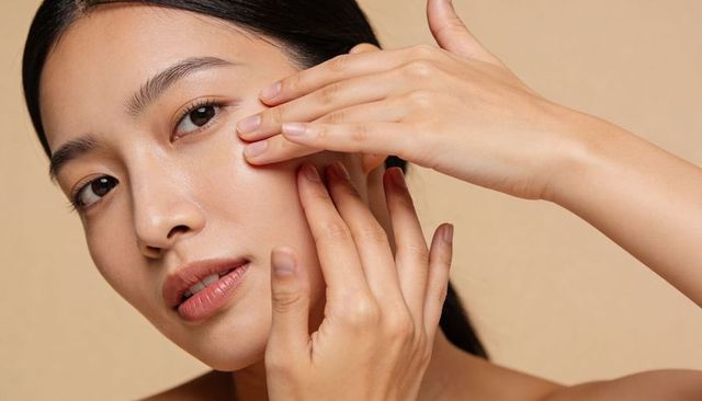 Asian woman applying skincare moisturizer on face closeup smooth glowing complexion