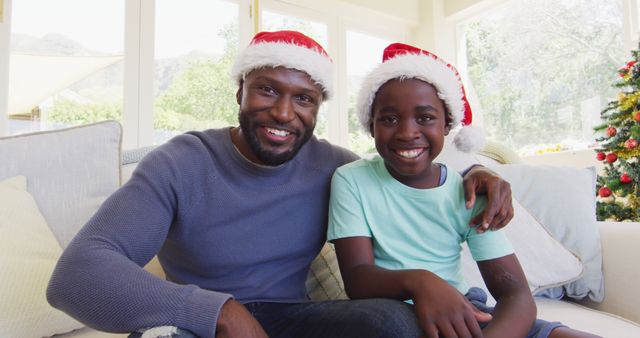 Father and son sitting on couch wearing Santa hats smiling - Download Free Stock Images Pikwizard.com