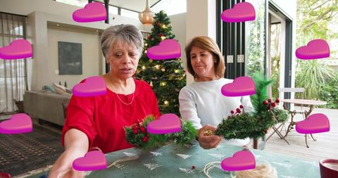 Women arranging christmas wreaths with greenery and crafts by decorated tree in living room