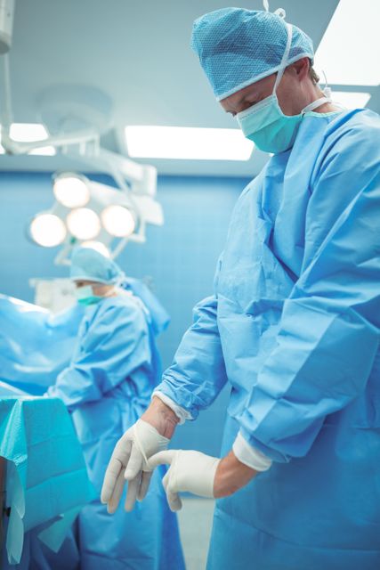 Male surgeon wearing surgical gloves in operation theater at hospital