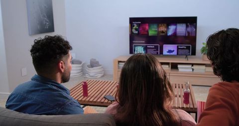 Friends watching streaming interface on couch with popcorn and drinks in cozy living room