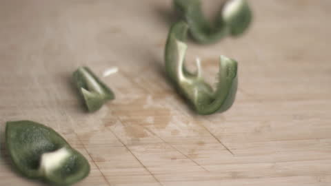 Green Pepper Slices Falling on Cutting Board in Slow Motion