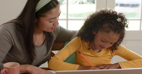 Caregiver tutoring daughter at home helping with homework and writing by window