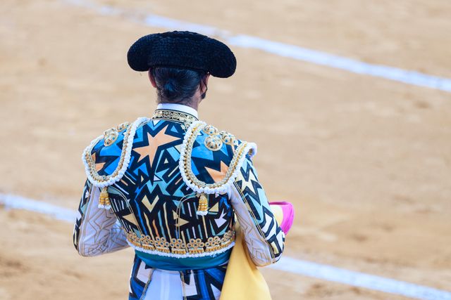 This stock photo depicts a bullfighter wearing a richly adorned traditional costume, standing in a bullring. The decorative costume stands out against the sandy bullring background. Ideal for use in materials discussing Spanish culture, traditional events, or enhancing travel brochures. Additionally, it is suitable for articles and educational content about bullfighting and its cultural significance.