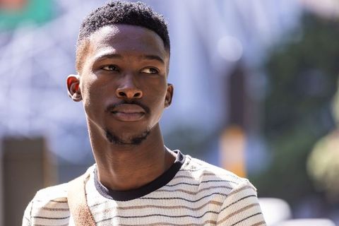 Thoughtful african man standing on urban street wearing striped shirt and bag in sunlight