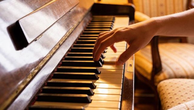 Intimate close-up right hand playing vintage upright piano keys in warm golden home light