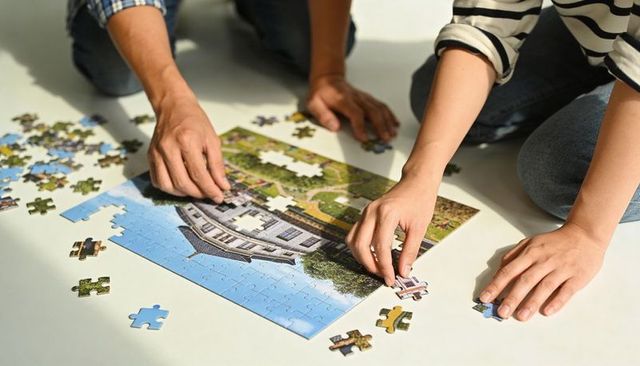 Couple assembling house jigsaw puzzle on white floor showing teamwork and home planning