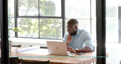 Focused Professional with Laptop and Architectural Plans in Modern Office