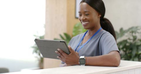Smiling african nurse using tablet at clinic reception wearing smartwatch and lanyard