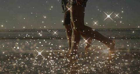 Walking couple splashing in shallow sea at sunset with sparkling bokeh and star flares