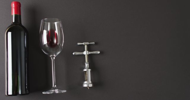 Red wine glass and corkscrew lying on black surface with copy space. Wine, alcohol, beverage and wine tasting concept.