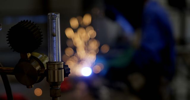 A close-up view of an industrial tool with a welder working in the background and sparks flying. Useful for portraying industrial, manufacturing, or engineering environments. Ideal for illustrating factory operations, industrial professions, or mechanical processes.