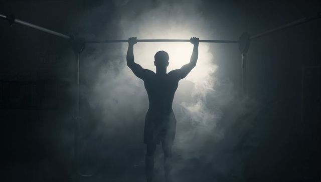 Silhouette athlete performing pull-up with dramatic backlight and fog