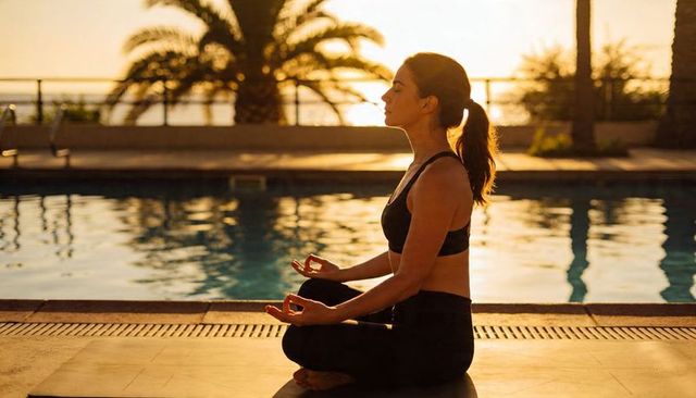 Woman meditating by pool at sunset practicing mindfulness and yoga
