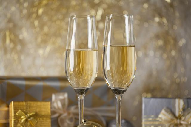 Two champagne flutes and Christmas gifts against golden color decoration